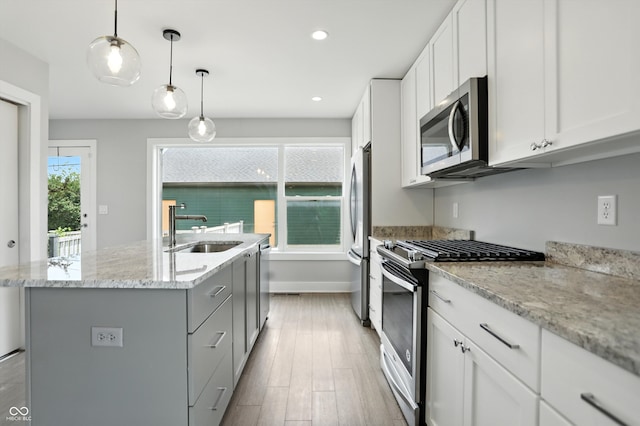 1905 Cornell Ave, Indianapolis, IN 46202 - kitchen featuring appliances with stainless steel finishes, a center island with sink, light wood-type flooring, white cabinets, and decorative light fixtures