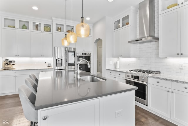 10795 Creekbed Cir, Fishers, IN 46038 - kitchen with wall chimney range hood, stainless steel appliances, arched walkways, tasteful backsplash, and a center island with sink