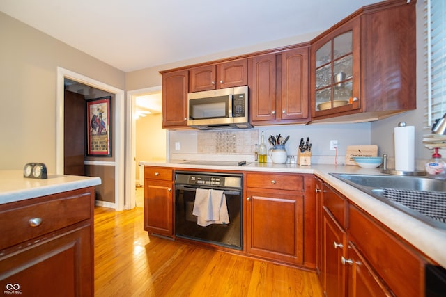 7224 N Tuxedo St, Indianapolis, IN 46240 - kitchen featuring black appliances, light wood-type flooring, light countertops, glass insert cabinets, and backsplash