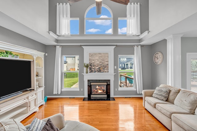 7830 Cross Crk, Avon, IN 46123 - living room featuring a towering ceiling, ceiling fan, light wood-type flooring, a fireplace with flush hearth, and ornate columns