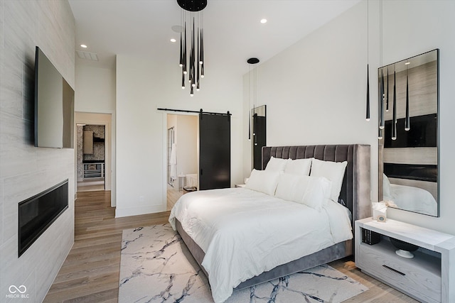 1269 Chatham Rdg Ct, Westfield, IN 46074 - bedroom featuring a barn door, light wood finished floors, recessed lighting, a glass covered fireplace, and a towering ceiling