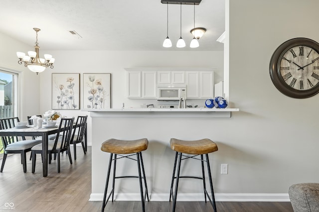 12404 Titans Dr, Fishers, IN 46037 - kitchen with white microwave, a chandelier, a kitchen bar, wood finished floors, and light countertops