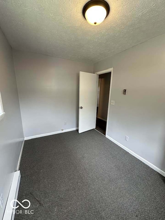 1941 W Booe Rd, Austin, IN 47102 - empty room featuring a textured ceiling, a baseboard radiator, and dark colored carpet
