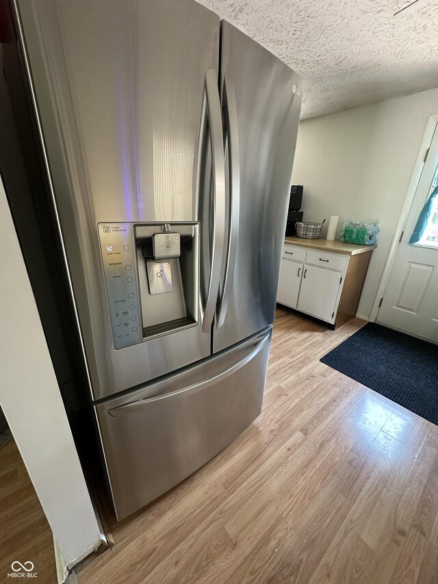 7607 Ardwell Ct, Indianapolis, IN 46237 - kitchen view of stainless steel fridge with ice dispenser, white cabinets, light wood-type flooring, light countertops, and a textured ceiling