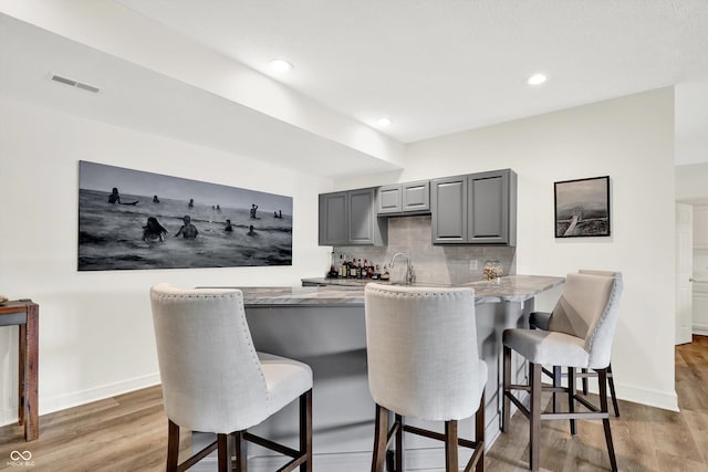11137 Peppermill Ln, Fishers, IN 46037 - kitchen with gray cabinetry, light wood-style floors, a breakfast bar area, backsplash, and recessed lighting