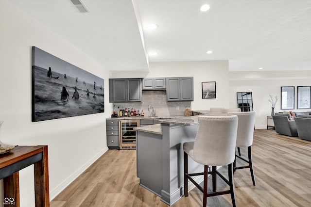 11137 Peppermill Ln, Fishers, IN 46037 - kitchen with wine cooler, gray cabinetry, a kitchen bar, backsplash, and light wood-style floors