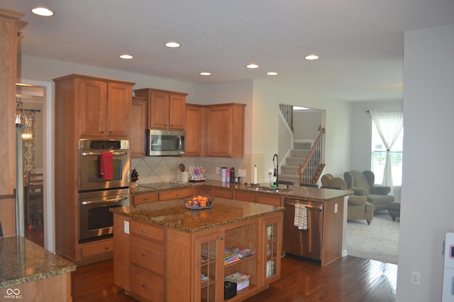 10166 Ranford Blvd, Fishers, IN 46040 - kitchen with appliances with stainless steel finishes, brown cabinetry, a peninsula, dark stone countertops, and recessed lighting