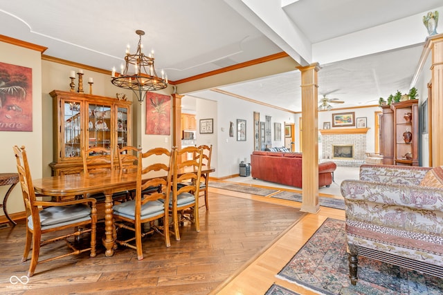 2320 Whispering Way, Indianapolis, IN 46239 - dining space featuring a brick fireplace, a chandelier, crown molding, ornate columns, and light wood finished floors