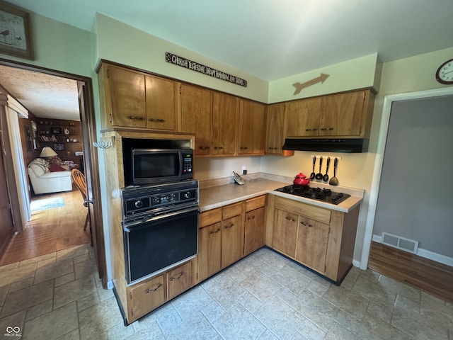4032 Roselawn Ave, Columbus, IN 47203 - kitchen with black appliances, under cabinet range hood, light countertops, light stone finish flooring, and brown cabinets