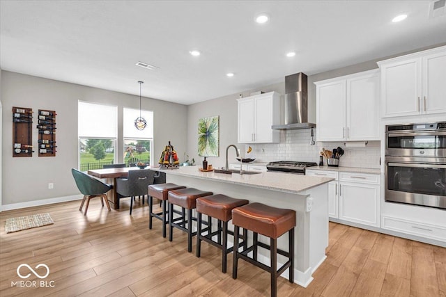 5345 Ridgecrest Ln, Mccordsville, IN 46055 - kitchen featuring wall chimney exhaust hood, stainless steel double oven, a kitchen island with sink, tasteful backsplash, and a breakfast bar