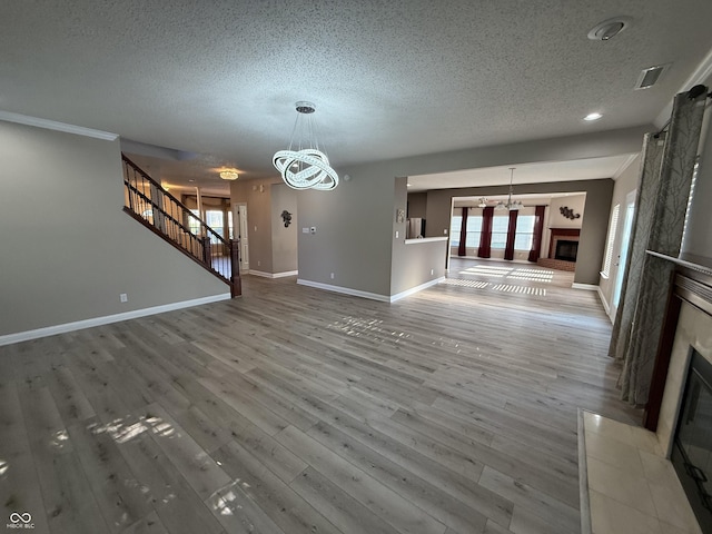 14171 Refreshing Garden Ln, Fishers, IN 46038 - unfurnished living room featuring a fireplace, a textured ceiling, a chandelier, stairs, and wood finished floors