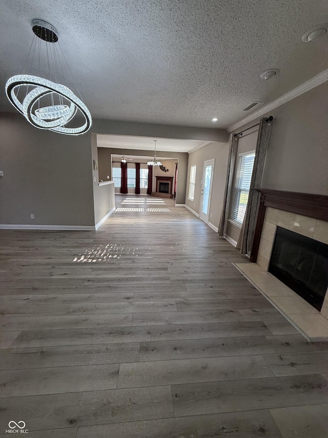 14171 Refreshing Garden Ln, Fishers, IN 46038 - unfurnished living room with a textured ceiling, a tile fireplace, a chandelier, wood finished floors, and crown molding