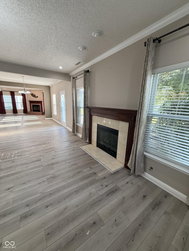 14171 Refreshing Garden Ln, Fishers, IN 46038 - unfurnished living room featuring a tile fireplace, a textured ceiling, wood finished floors, ornamental molding, and a chandelier