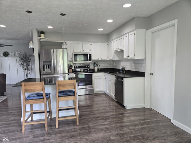 8401 Culpeper Dr, Indianapolis, IN 46227 - kitchen featuring stainless steel appliances, dark countertops, dark wood-type flooring, white cabinetry, and hanging light fixtures