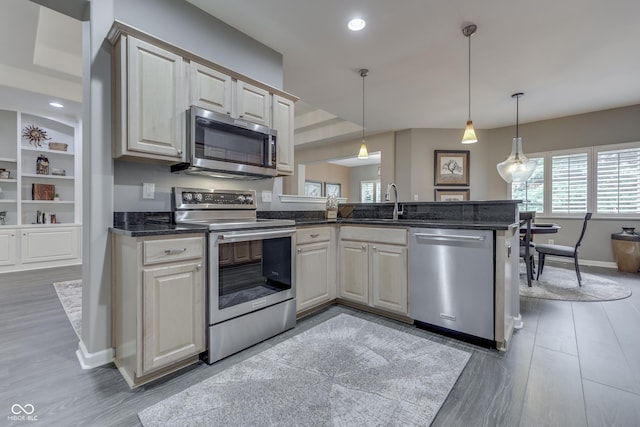 1454 Heron Ridge Blvd, Greenwood, IN 46143 - kitchen featuring stainless steel appliances, a peninsula, wood finished floors, hanging light fixtures, and dark stone countertops