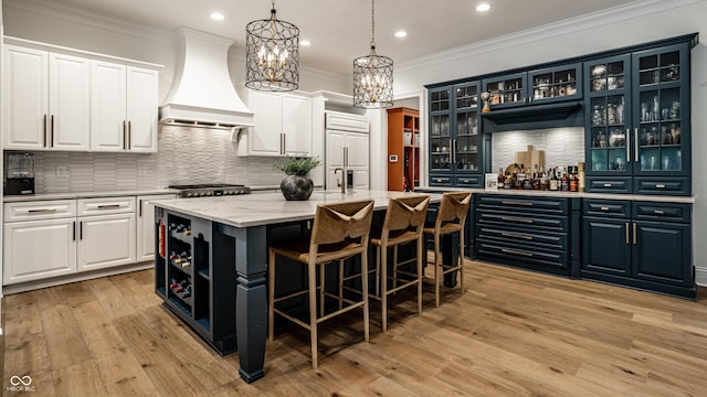 9681 Pleasant View Ln, Zionsville, IN 46077 - kitchen with custom range hood, crown molding, a kitchen island with sink, a chandelier, and white cabinets