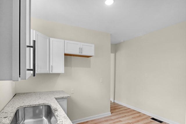 kitchen with light stone countertops, white cabinets, and light wood-style flooring
