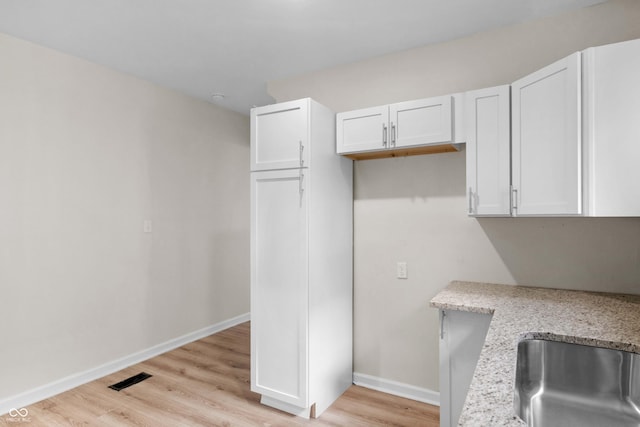kitchen with white cabinetry, light wood-style flooring, and light stone counters