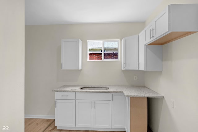 kitchen with light stone counters, light wood finished floors, and white cabinets