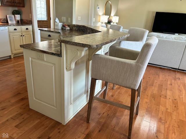 2080 Galway Trl N, Madison, IN 47250 - kitchen with dark countertops, light wood finished floors, a kitchen bar, white dishwasher, and a peninsula