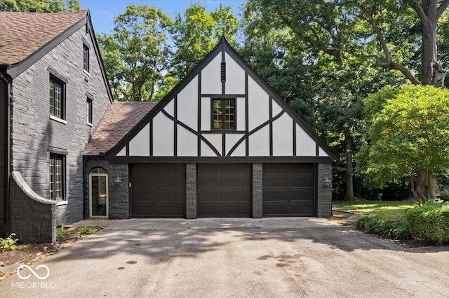 6470 Around The Hills Rd, Indianapolis, IN 46226 - tudor home featuring roof with shingles, stone siding, and driveway