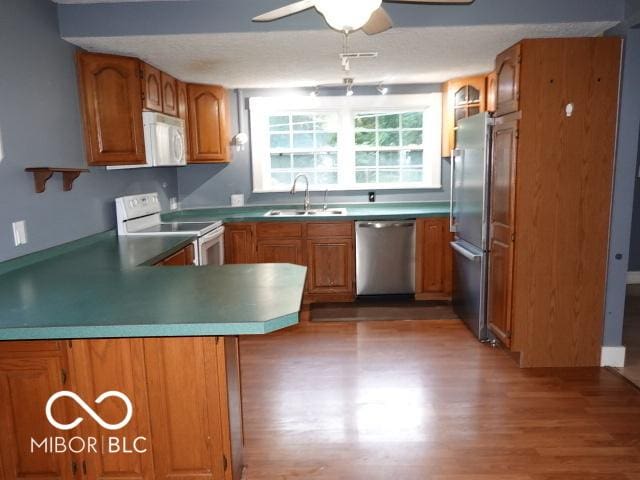 kitchen featuring appliances with stainless steel finishes, a peninsula, brown cabinetry, and wood finished floors