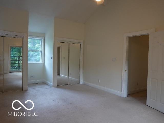 unfurnished bedroom featuring carpet, two closets, and lofted ceiling