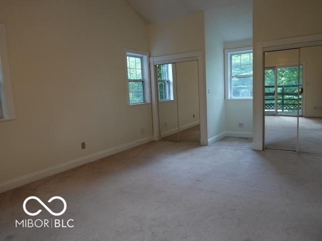 unfurnished bedroom featuring carpet, vaulted ceiling, and two closets