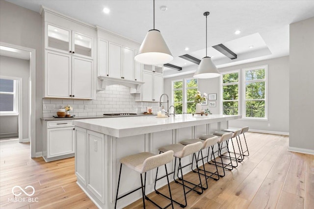 2840 Flowing Creek Pl, Westfield, IN 46074 - kitchen featuring cooktop, white cabinetry, tasteful backsplash, a center island with sink, and light wood-style flooring
