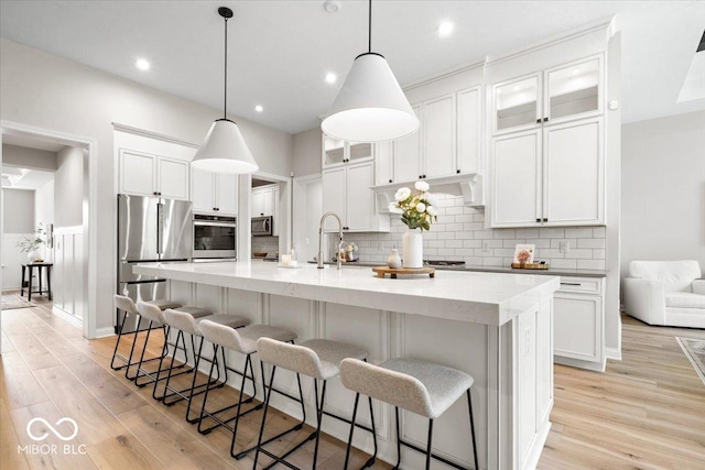 2840 Flowing Creek Pl, Westfield, IN 46074 - kitchen with appliances with stainless steel finishes, light wood finished floors, white cabinetry, a large island with sink, and a kitchen bar
