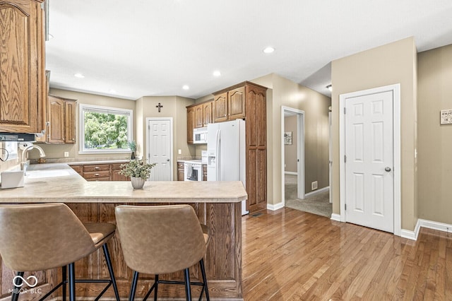 11 Stratford Way, Danville, IN 46122 - kitchen featuring white appliances, light wood-style flooring, a peninsula, a breakfast bar area, and light countertops