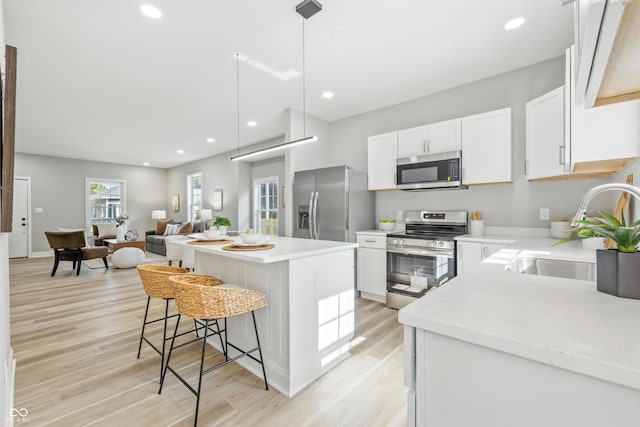 2012 N Dexter St, Indianapolis, IN 46202 - kitchen with appliances with stainless steel finishes, light wood-style flooring, a center island, a kitchen breakfast bar, and white cabinetry