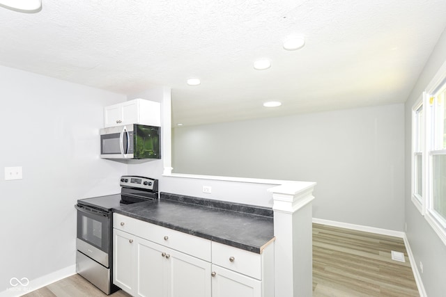 2521 Winfield Ave, Indianapolis, IN 46222 - kitchen with stainless steel appliances, dark countertops, light wood-type flooring, white cabinets, and a peninsula
