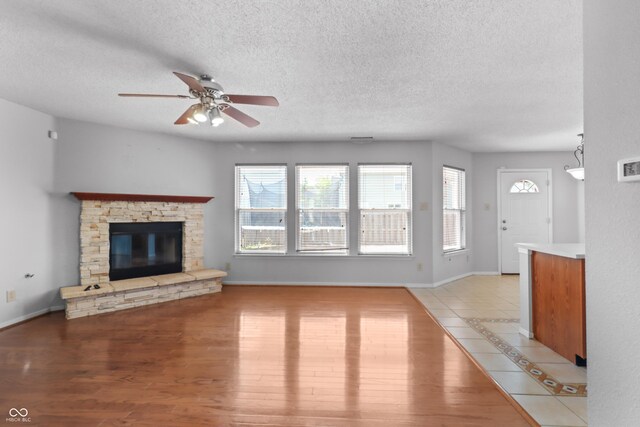 12443 Rose Haven Dr, Indianapolis, IN 46235 - unfurnished living room featuring healthy amount of natural light, a ceiling fan, a stone fireplace, a textured ceiling, and light wood finished floors