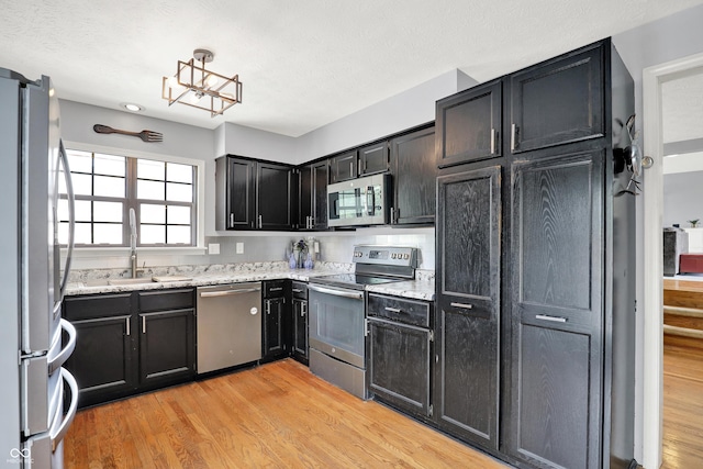 826 Royal Saint George Dr, Greenwood, IN 46143 - kitchen featuring appliances with stainless steel finishes, light wood-style floors, light stone countertops, dark cabinetry, and a chandelier