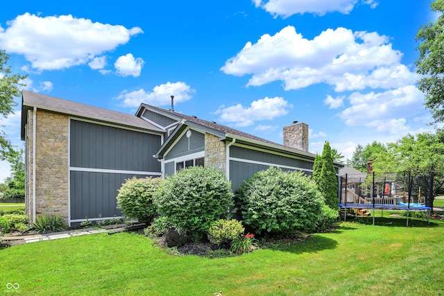 826 Royal Saint George Dr, Greenwood, IN 46143 - view of side of property featuring stone siding, a trampoline, a lawn, and a chimney