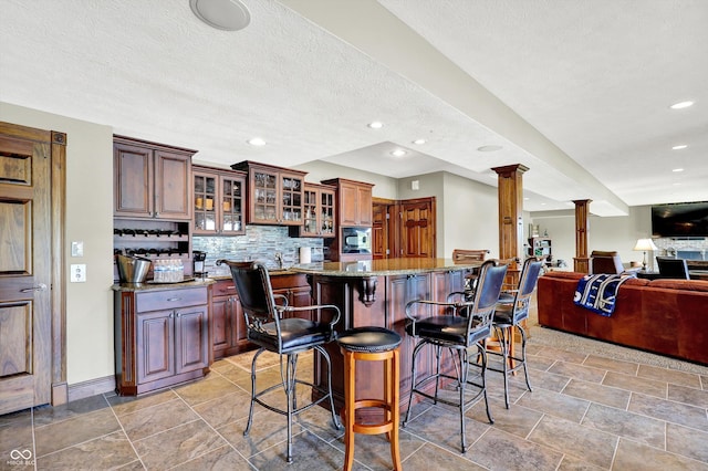 523 S 700 E, Whitestown, IN 46075 - kitchen with ornate columns, light stone counters, decorative backsplash, a breakfast bar area, and a kitchen island