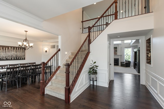 10334 Strongbow Rd, Fishers, IN 46040 - stairway with a chandelier, wood finished floors, crown molding, a decorative wall, and a glass covered fireplace