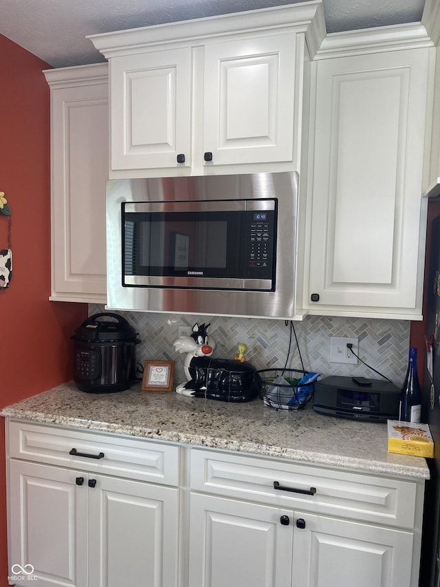 1675 Leisure Way, Greenfield, IN 46140 - kitchen featuring stainless steel microwave, decorative backsplash, white cabinetry, and light stone counters
