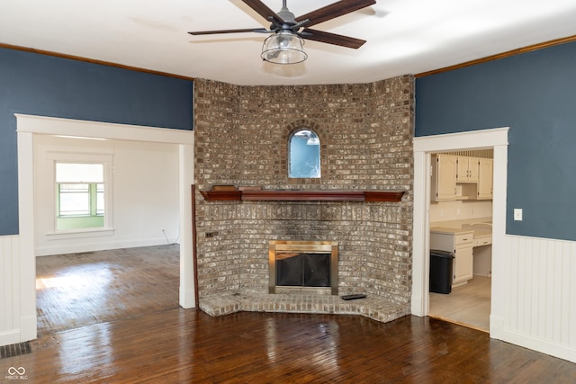 602 Valley Dr, Crawfordsville, IN 47933 - unfurnished living room with a ceiling fan, wood finished floors, wainscoting, a brick fireplace, and crown molding