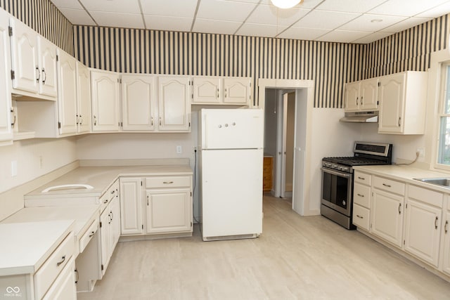 602 Valley Dr, Crawfordsville, IN 47933 - kitchen featuring freestanding refrigerator, stainless steel gas range, under cabinet range hood, a paneled ceiling, and white cabinetry