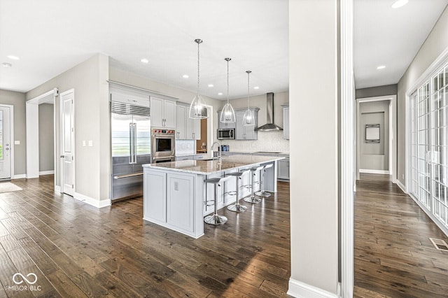 14293 Dufton Ct, Carmel, IN 46074 - kitchen featuring stainless steel appliances, wall chimney range hood, a breakfast bar area, dark wood-type flooring, and recessed lighting
