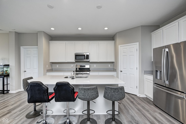8108 Nik St, Brownsburg, IN 46112 - kitchen featuring stainless steel appliances, light wood finished floors, light countertops, a kitchen island with sink, and a breakfast bar area