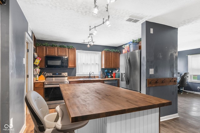 43 W Main St, North Vernon, IN 47265 - kitchen featuring stainless steel appliances, butcher block countertops, wood finished floors, a textured ceiling, and brown cabinets
