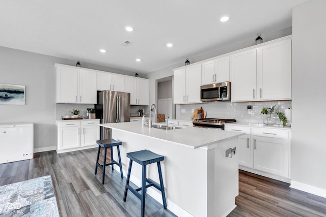 9978 Trafford Ct, Mccordsville, IN 46055 - kitchen with appliances with stainless steel finishes, a kitchen island with sink, tasteful backsplash, wood finished floors, and recessed lighting