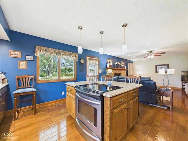 1014 Gray Squirrel Dr, Pendleton, IN 46064 - kitchen with stainless steel electric stove, a fireplace, hardwood / wood-style flooring, brown cabinetry, and ceiling fan
