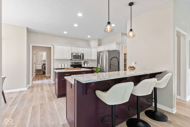 5910 Hickory Woods Dr, Plainfield, IN 46168 - kitchen featuring stainless steel appliances, light wood-style flooring, decorative backsplash, light stone countertops, and a kitchen breakfast bar