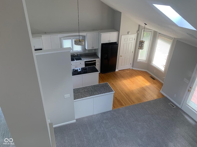 9532 Pinecreek Dr, Indianapolis, IN 46256 - kitchen with black appliances, light carpet, white cabinetry, a skylight, and hanging light fixtures