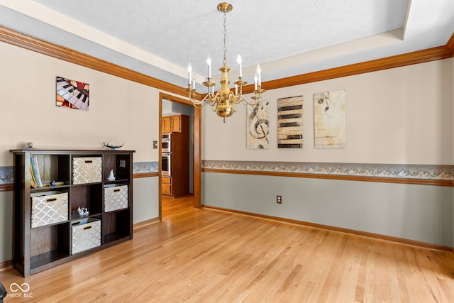 7621 Forest Dr, Fishers, IN 46038 - unfurnished dining area with a chandelier, a tray ceiling, wood finished floors, a textured ceiling, and crown molding