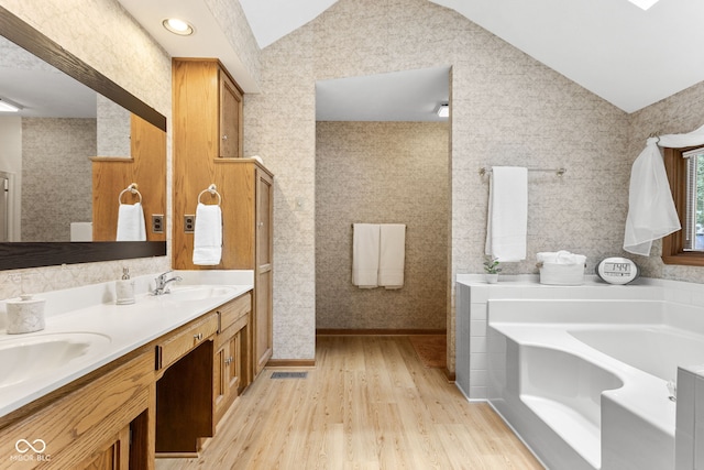 7621 Forest Dr, Fishers, IN 46038 - bathroom featuring vaulted ceiling, a bath, wood finished floors, and double vanity